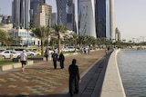 Huge towers dominate the Doha CBD skyline while people walk along a footpath.