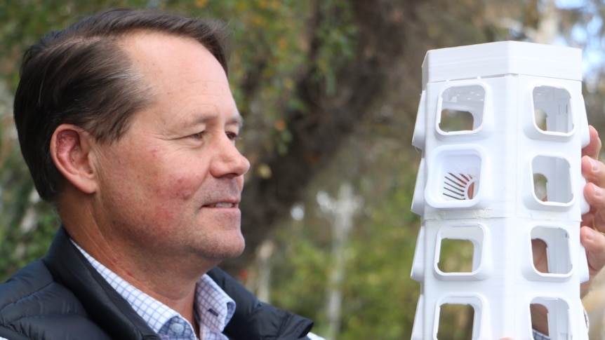 Paul Millet from Invertigro vertical farm company holding one of the wall segments with tree behind.