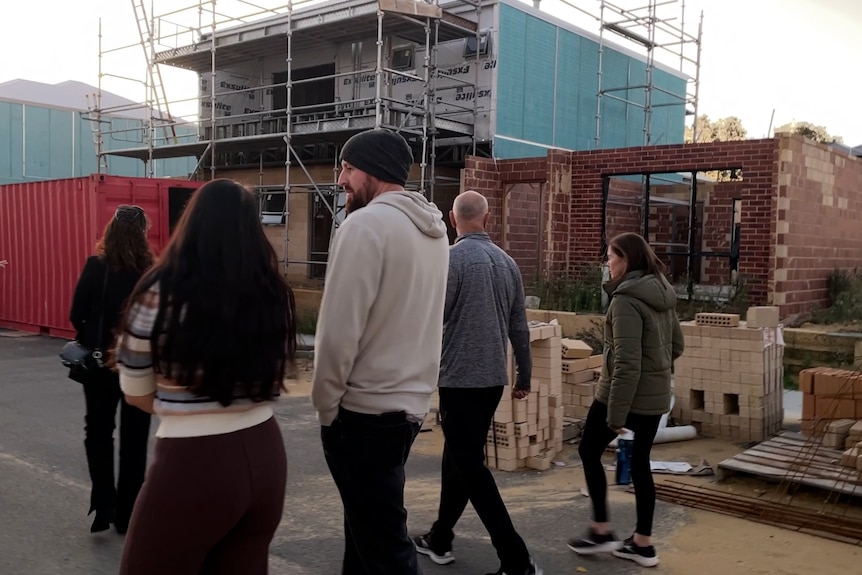 A group of people standing in the street, with unfinished houses in the background.