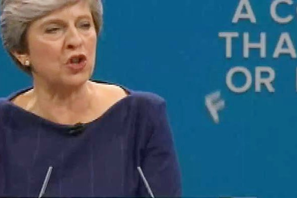 A sign falls apart behind Theresa May