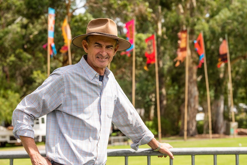 A man in a hat smiles with trees and colourful flags in the background.