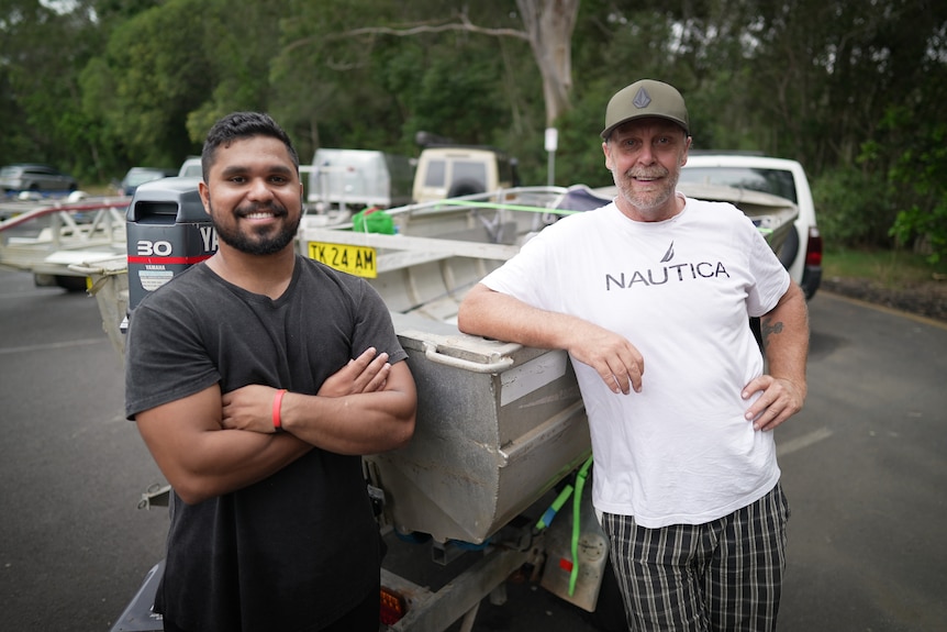 Leeroy stands grinning with his arms crossed, while Brett leans his elbow on a boat and laughs.