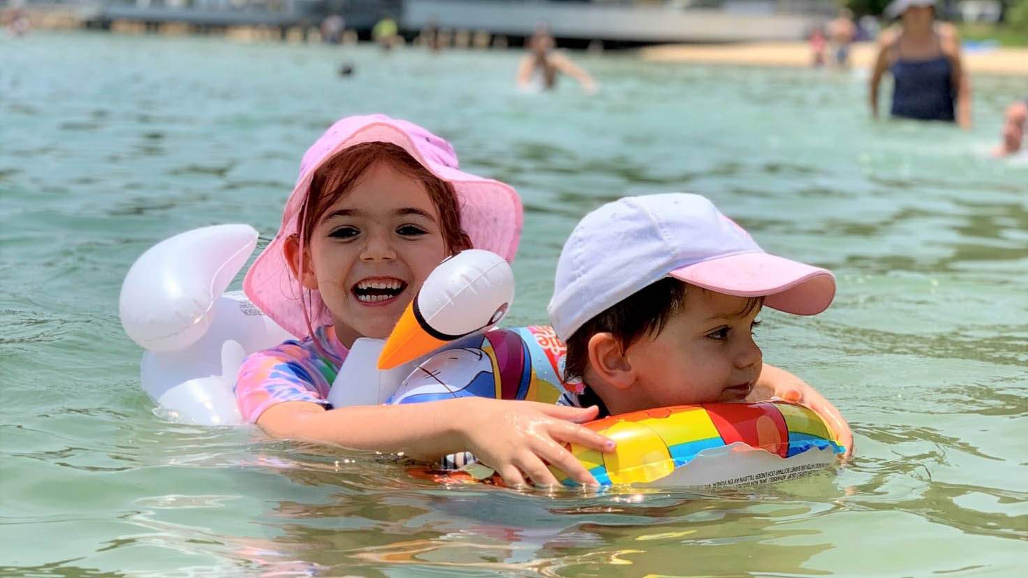 A girl and a boy swimming at the beach using floaties