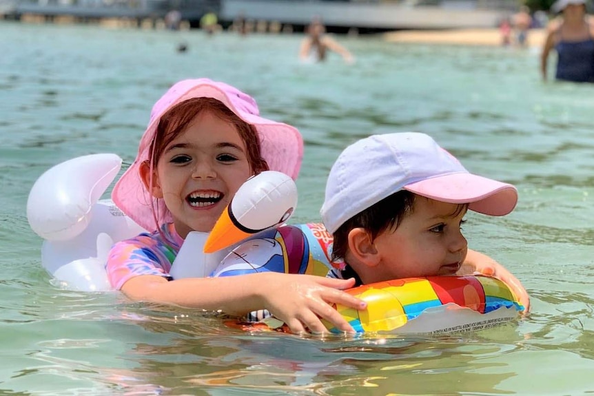 A girl and a boy swimming at the beach using floaties