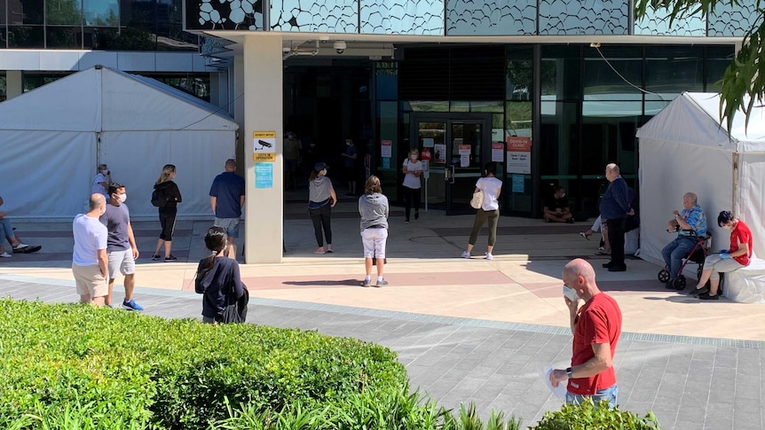 People standing around wearing face masks in front of a modern building