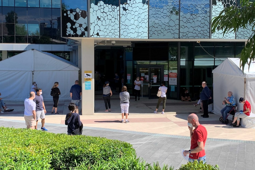 People standing around wearing face masks in front of a modern building