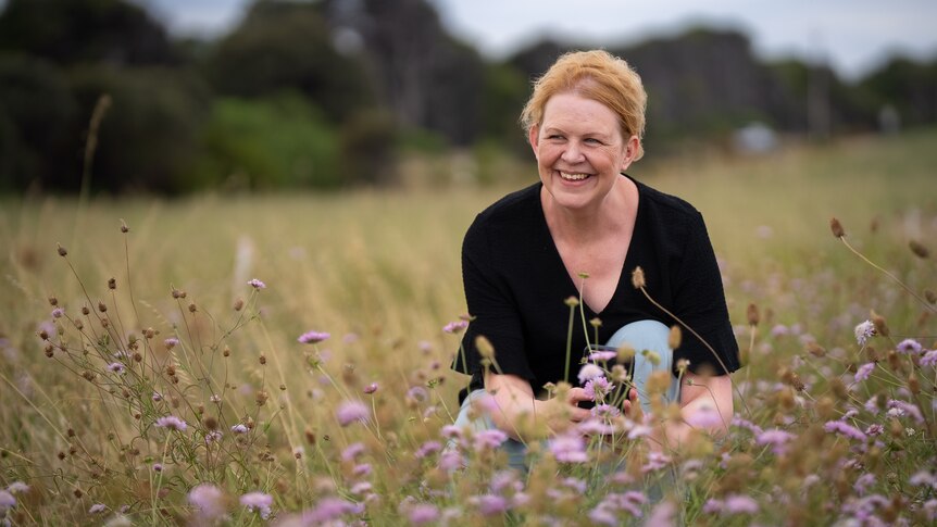A woman with strawberry blonde hair smiles in a field of flowers.
