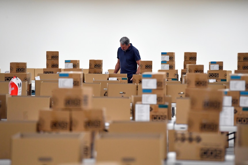 Stacks of boxes sit on rows of tables, a worker visible in the background.