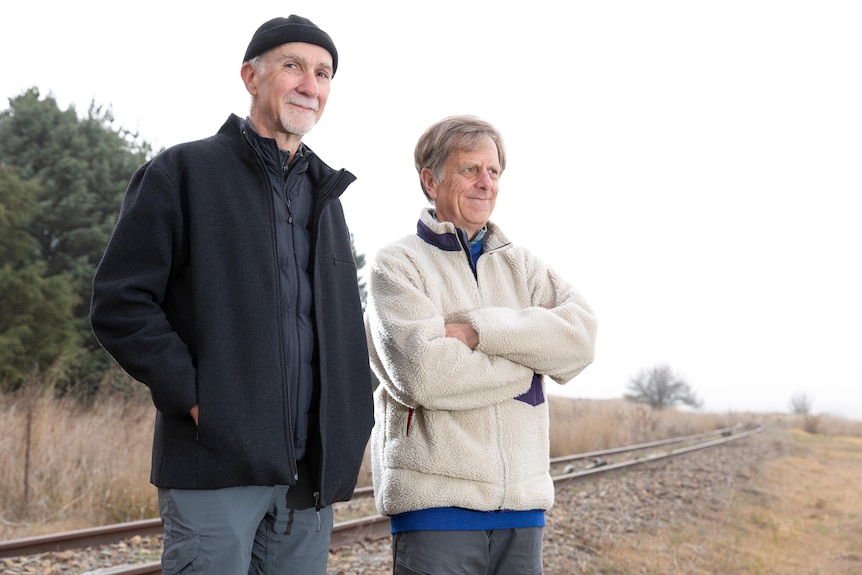 Two middle-aged men standing beside a rail line
