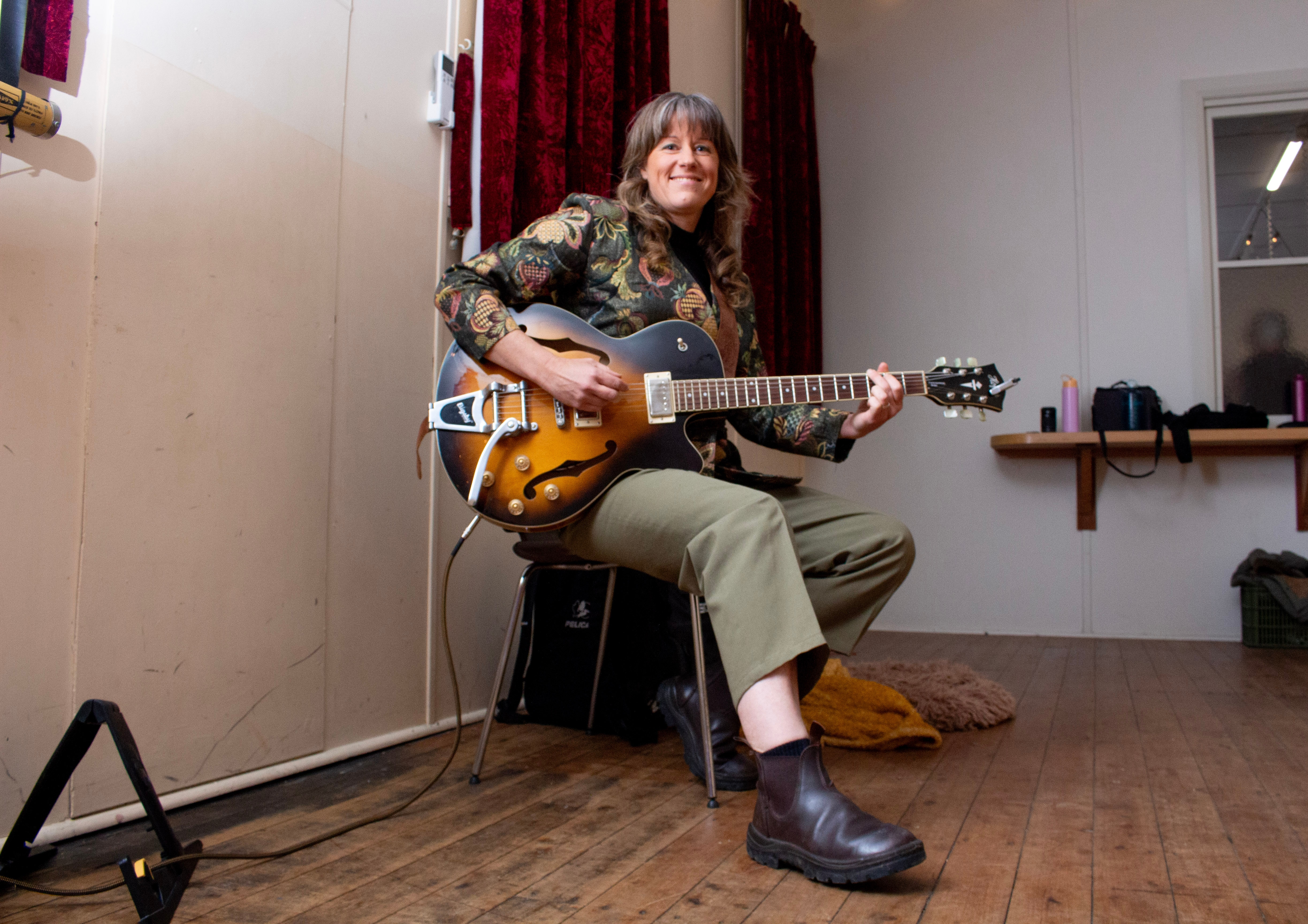 A woman smiles while playing a guitar.