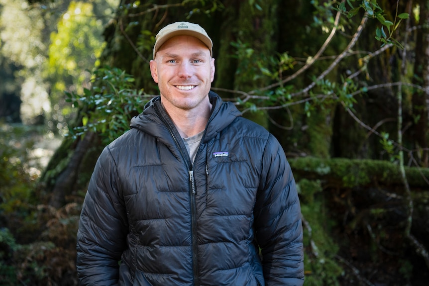 A man wearing a puffer jacket and a cap smiles for the camera 