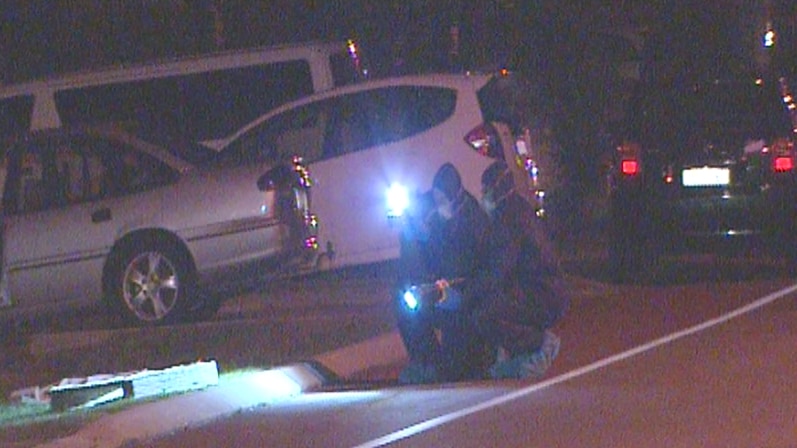 Forensic police crouch with a flashlight at the scene of a stabbing on Amelia Street in Balcatta.