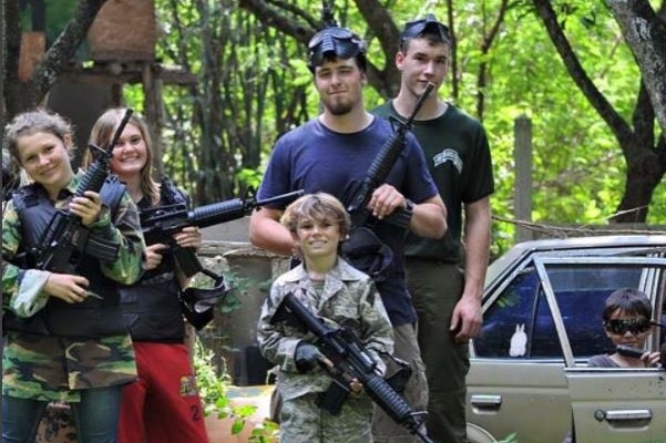 Five young people smile while holding guns