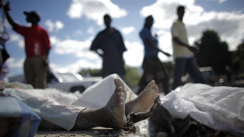 Residents walk next to a dead body after an earthquake in Port-au-Prince January 13, 2010