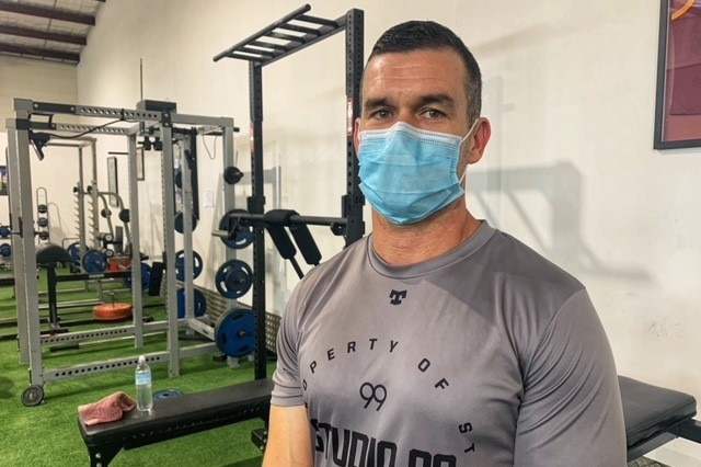 Personal trainer Matt Tranter wearing a mask stands in front of gym equipment.