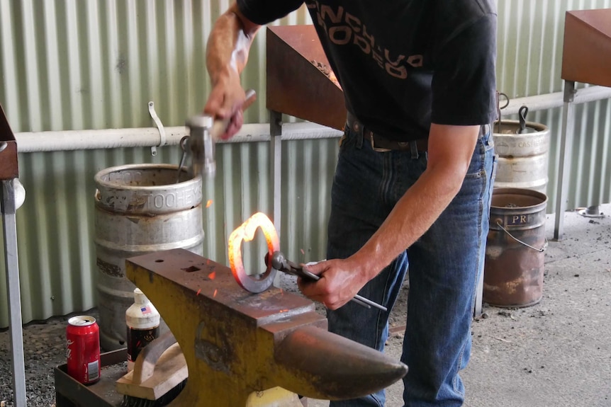 Man hits a molten horseshoe with a hammer held above an anvil.