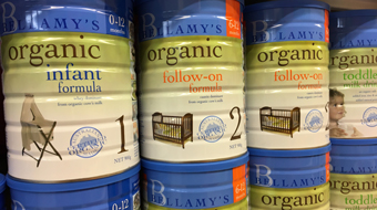 Four blue, white and green tins of infant formula on a shelf 
