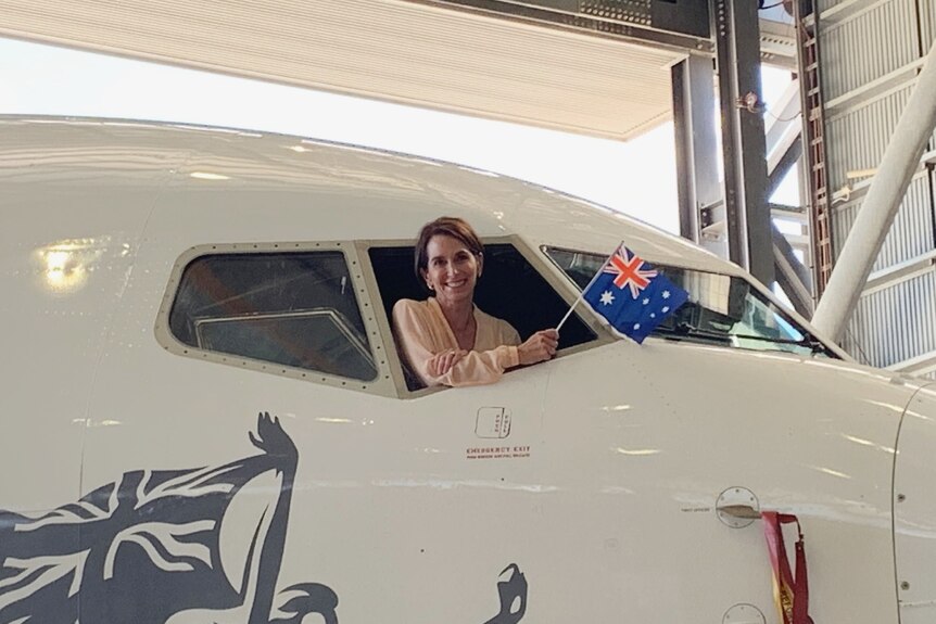 Virgin CEO Jayne Hrdlicka sits in the cockpit of a plane, waving an Australian flag.