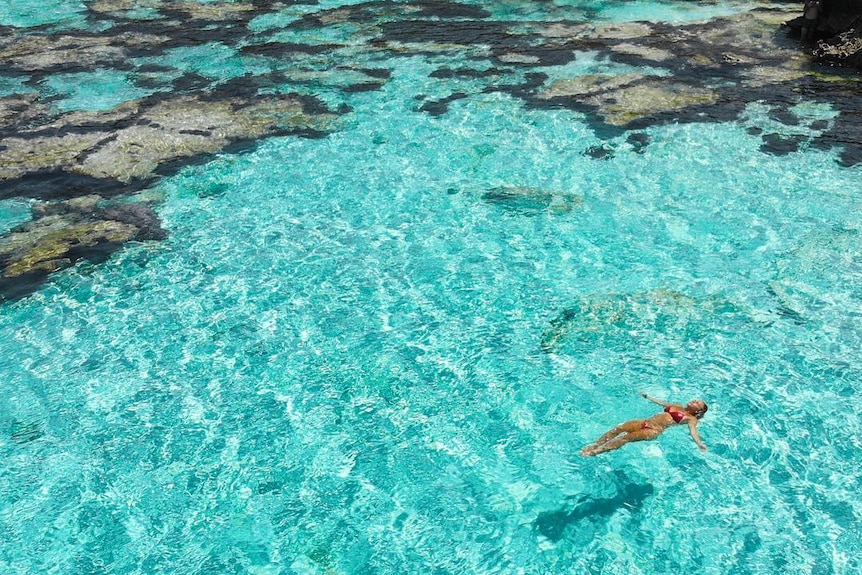 A woman floats in clear blue water.