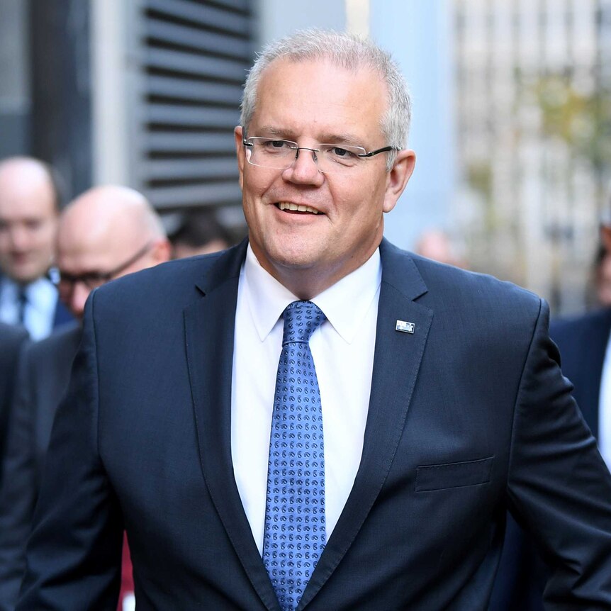 PM in a navy suit walks down a CBD street smiling