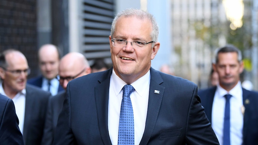 PM in a navy suit walks down a CBD street smiling