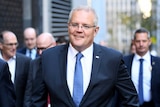 PM in a navy suit walks down a CBD street smiling