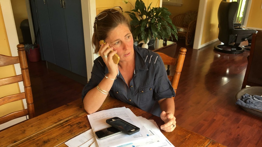 Woman on phone, sitting at kitchen table covered with paperwork