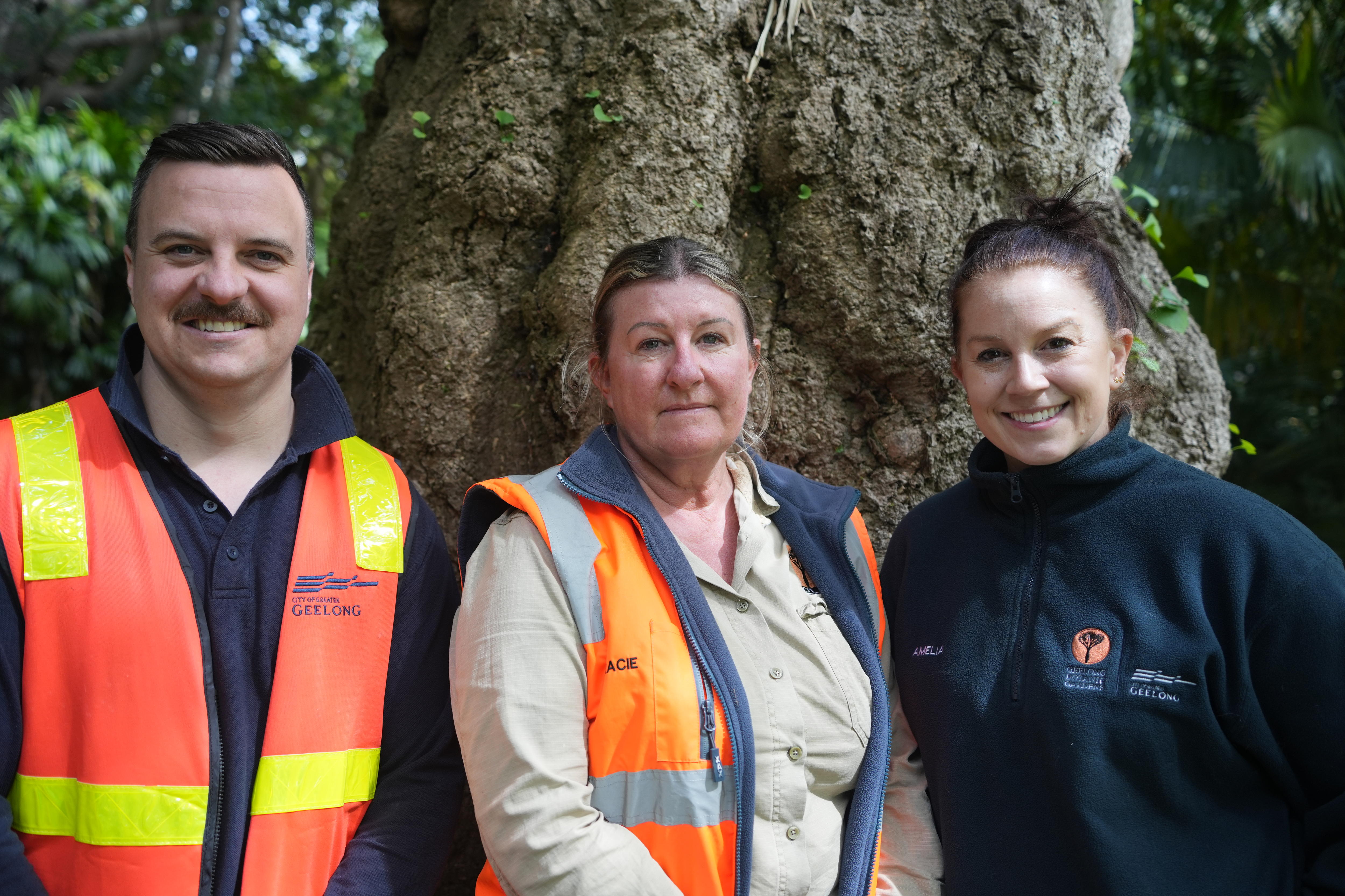 A man and two women stand in front of a ginkgo biloba tree trunk and smile.