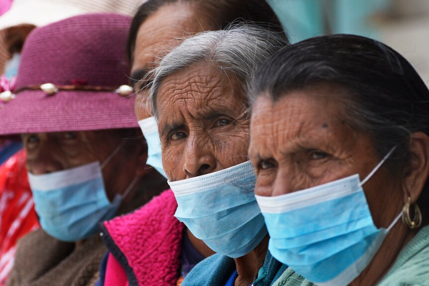 A row of older Mexican women wearing blue and white surgical face masks.