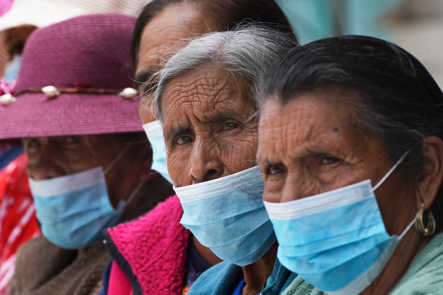 A row of older Mexican women wearing blue and white surgical face masks.