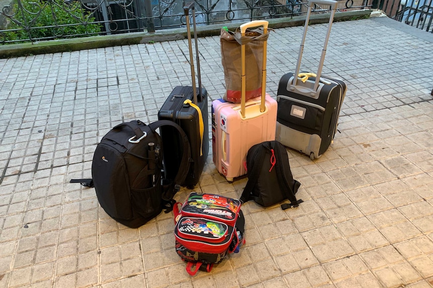 Photo of three suitcases, two backpacks and a tote bag.