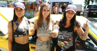 Three young women pose by a car.