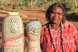 A woman standing with her pottery art work in front of hills south of Alice Springs