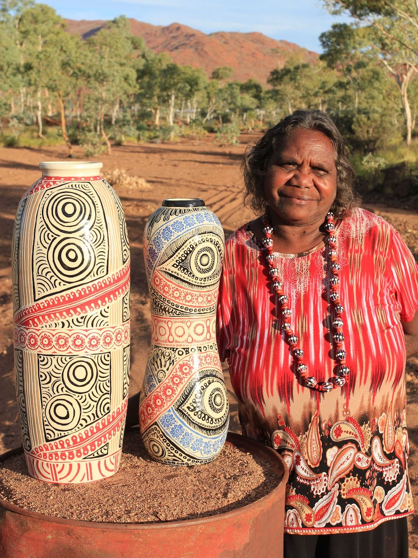 A woman standing with her pottery art work in front of hills south of Alice Springs