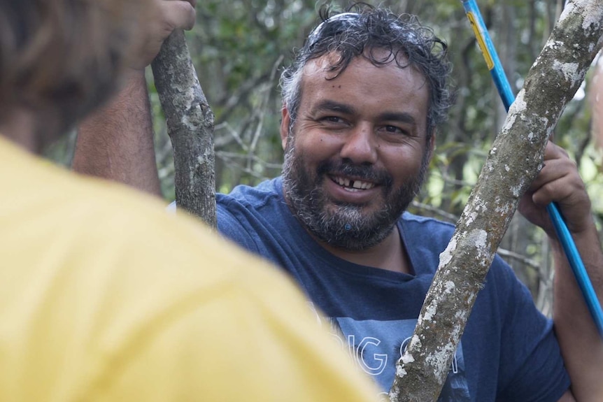 A man smiling and holding a spear in mangroves.
