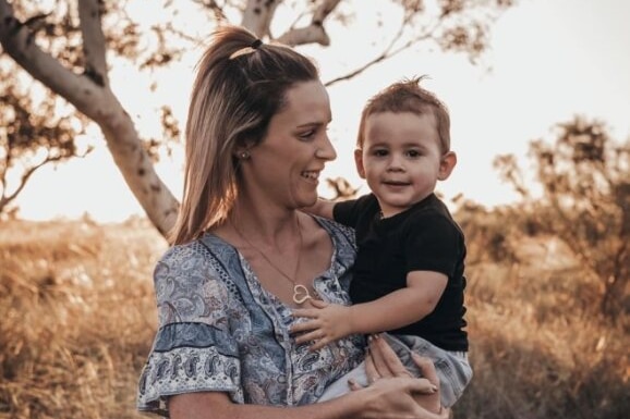 Woman smiling at her son, who she is holding. They are standing outdoors in a field.