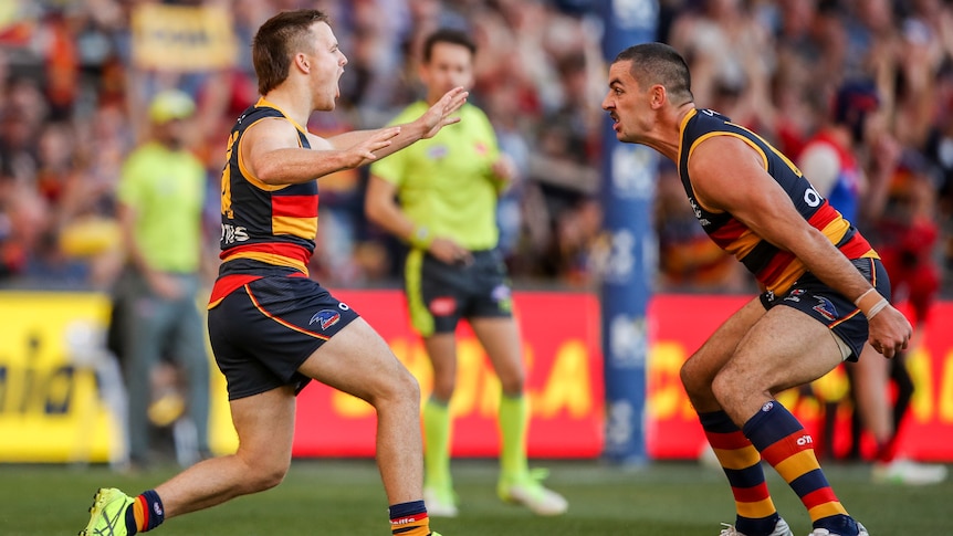 Two Adelaide Crows AFL players yell out at each other as they celebrate a goal.