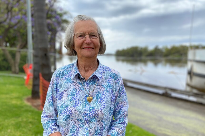 An older woman smiling at the camera with a collared shirt and river behind her.