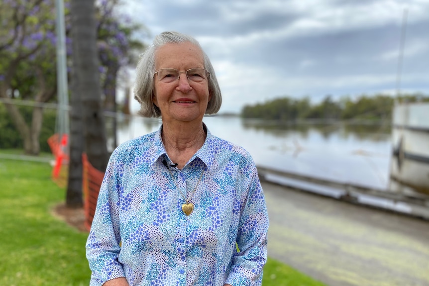 An older woman smiling at the camera with a collared shirt and river behind her.