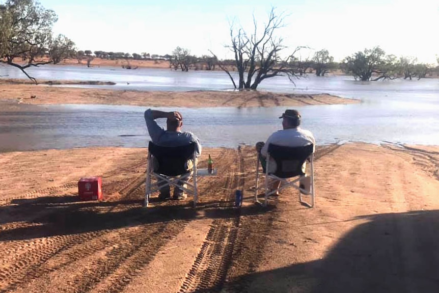 Two men sitting in camp chairs and staring at an expanse of flooded outback