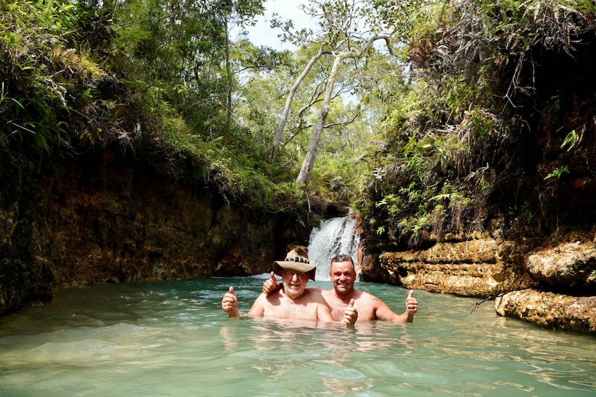 Two men giving the thumbs up while swimming in a waterhole in Cape York.