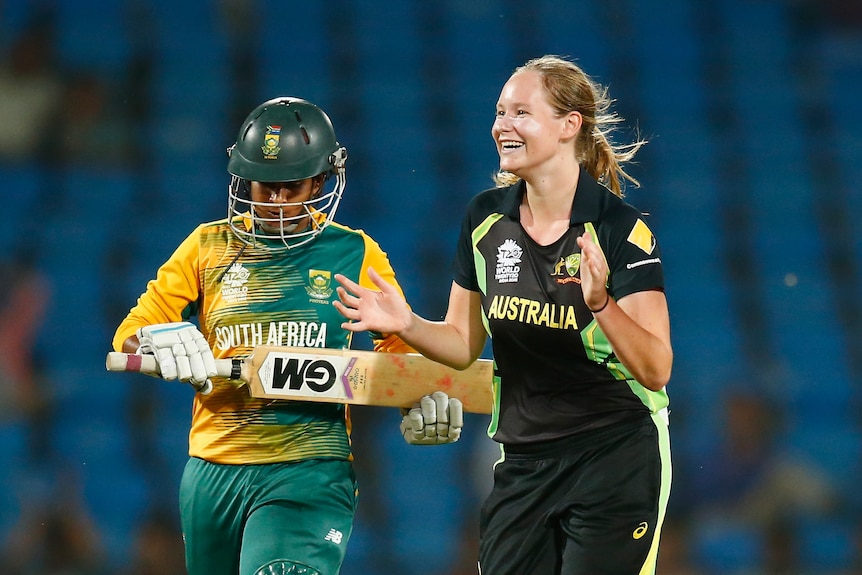 Lauren Cheatle smiles and claps as a batswoman walks off the pitch.