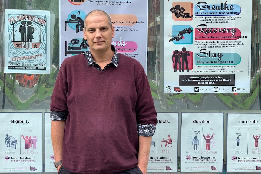 A man in a red jumper with his hands in his pockets in front of a large window with information on it about drug dependence.