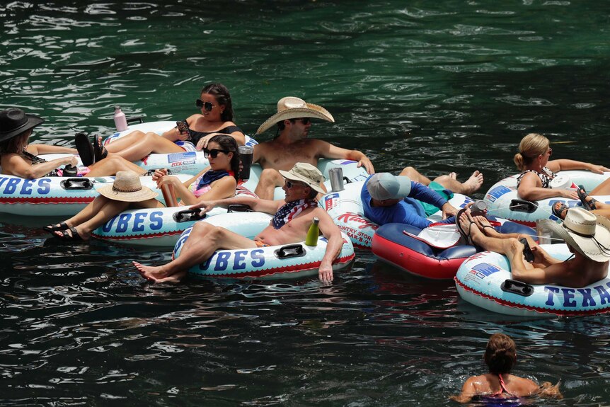 People in bathing suits ride rafts down a river, while in close proximity.