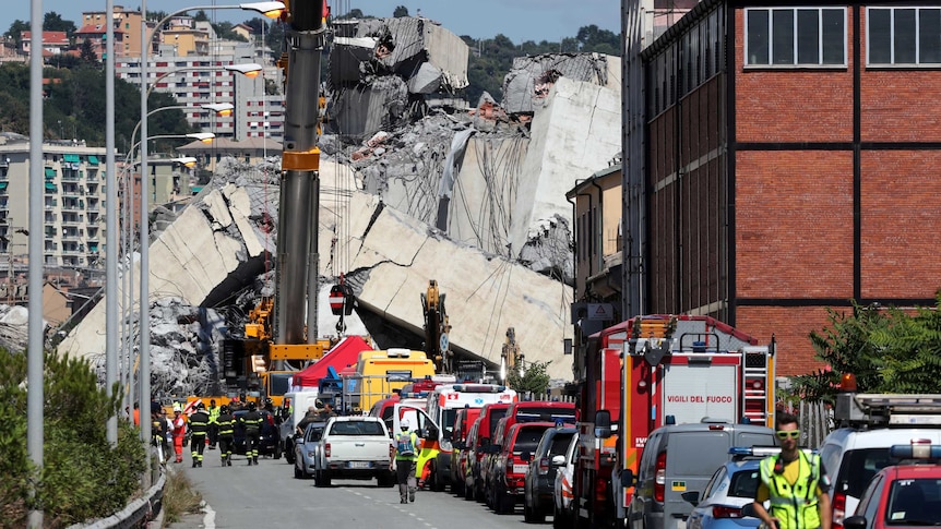 A wide shot shows huge collapsed concrete slabs and many emergency workers and vehicles.