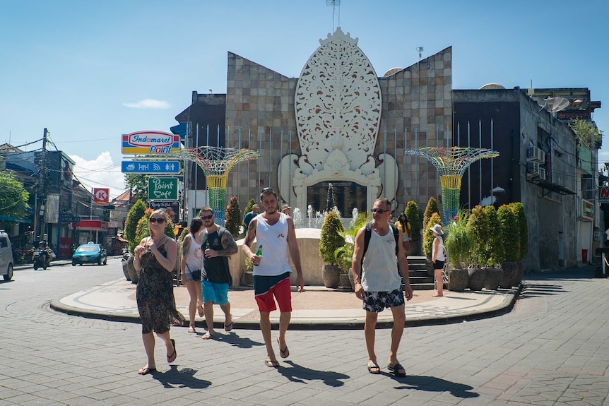 Tourists holding beers walk in front of the Bali bombing memorial site