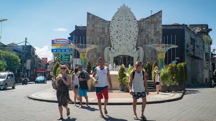 Tourists holding beers walk in front of the Bali bombing memorial site