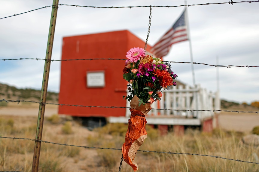 A bouquet of flowers on a barbed-wire fence in front of a red shed and American flag.