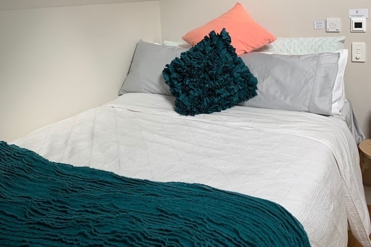 A bed with white sheets and a green blanket in a small dormitory room