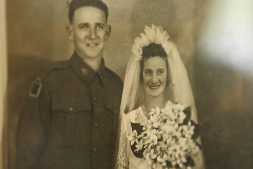 Black and white image of a serviceman in uniform and a bride with a white veil and large bunch of flowers.
